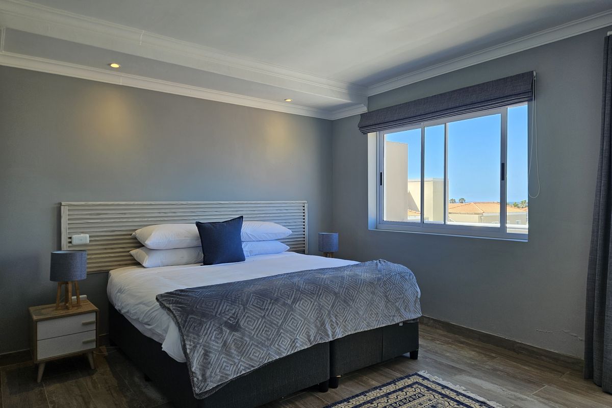 A well-maintained bedroom featuring wood-look tile flooring, recessed ceiling lighting, crown molding, and a built-in headboard with a view of the surrounding area.
