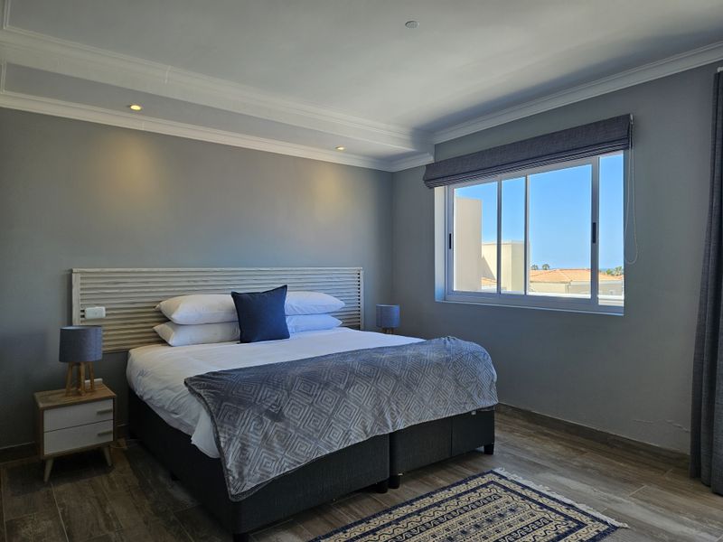A well-maintained bedroom featuring wood-look tile flooring, recessed ceiling lighting, crown molding, and a built-in headboard with a view of the surrounding area.