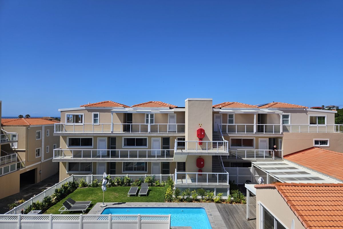 Exterior view of an apartment complex featuring a swimming pool, landscaped garden, and multiple levels of balconies with glass balustrades.