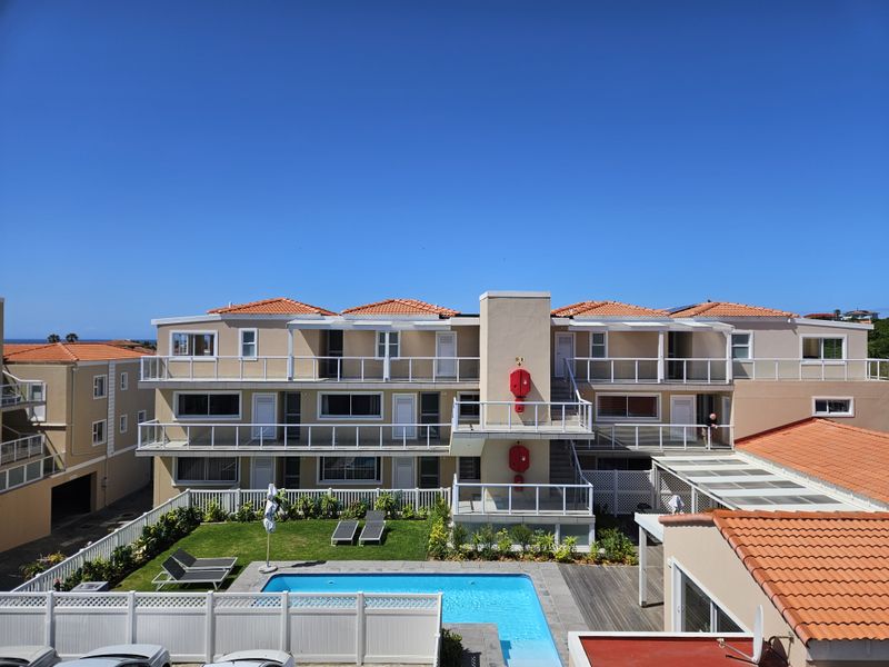 Exterior view of an apartment complex featuring a swimming pool, landscaped garden, and multiple levels of balconies with glass balustrades.