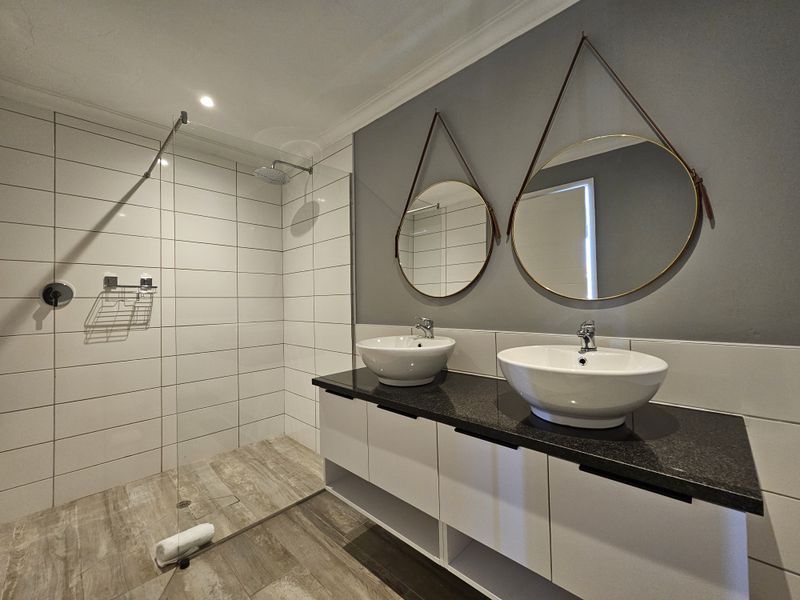 Modern bathroom featuring a double vanity with vessel sinks, granite countertop, and a spacious walk-in shower with a glass screen.