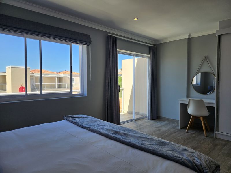 A well-lit bedroom featuring laminate flooring, built-in wardrobe, and sliding glass doors providing access to a private balcony.