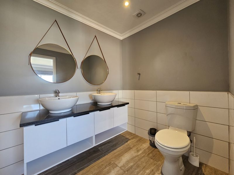 Modern bathroom featuring a double vanity with vessel sinks, granite countertop, white cabinetry, and neutral wall tiling.