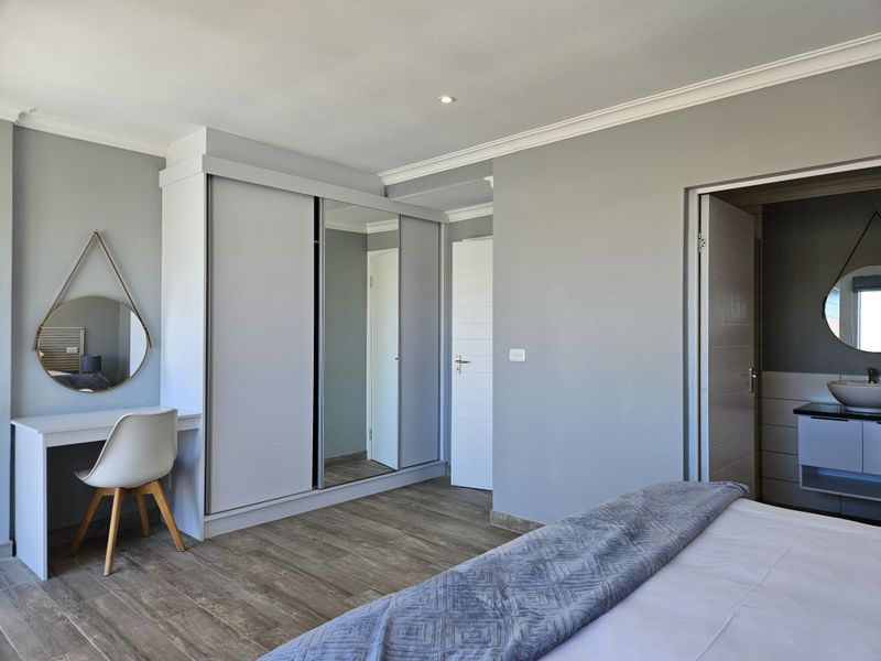 A well-maintained bedroom featuring built-in wardrobes with mirrored panels, wood-look laminate flooring, and direct access to an en-suite bathroom.
