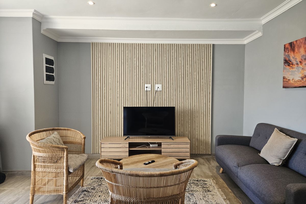 A well-maintained living room featuring a modern timber slat feature wall, recessed downlighting, and neutral tiled flooring.