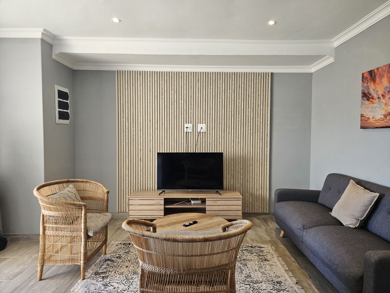 A well-maintained living room featuring a modern timber slat feature wall, recessed downlighting, and neutral tiled flooring.