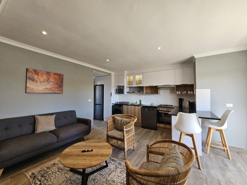 Modern open-plan living area featuring a well-equipped kitchen with built-in cabinetry, gas hob, oven, and a breakfast bar, seamlessly flowing into the lounge space.
