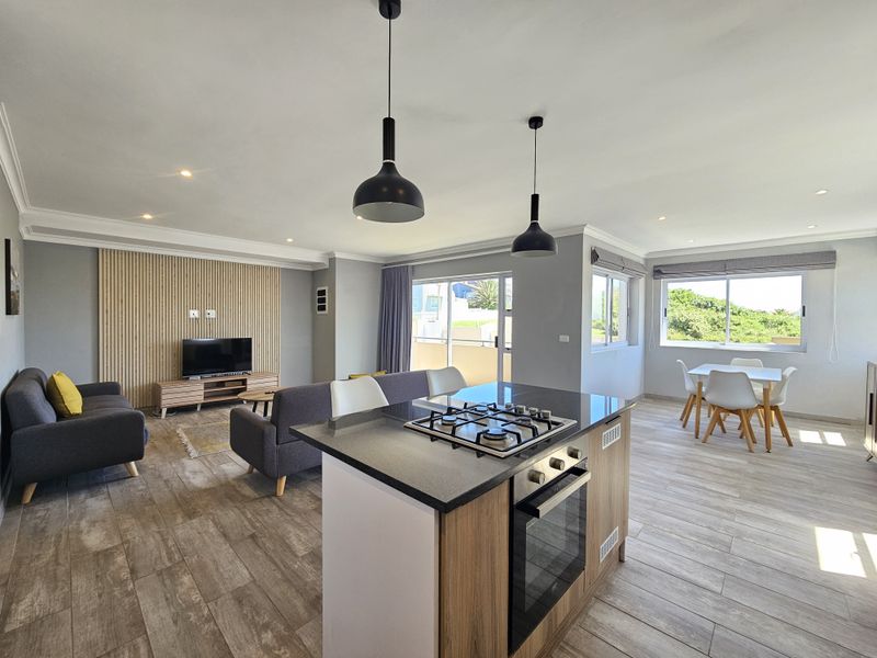 Modern open-plan living area featuring a kitchen island with gas hob, wood-look tile flooring, and a stylish slatted wood feature wall.