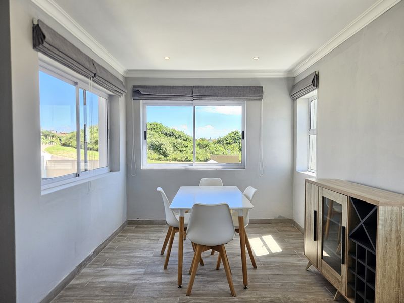 A bright dining area featuring tiled flooring, recessed downlights, and large sliding windows that provide natural light and views of the surrounding greenery.