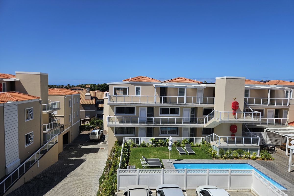 An elevated view of the apartment complex rear courtyard featuring a swimming pool, paved driveway, and multi-level balconies with white railings.