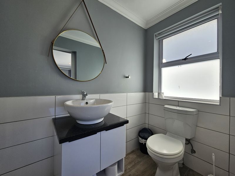 A modern bathroom featuring a vessel sink on a granite-topped vanity, a toilet, and a frosted window with tiled wall finishes.