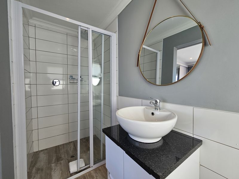 Modern bathroom featuring a glass-enclosed shower, a sleek vanity with a granite countertop, and a contemporary vessel sink.