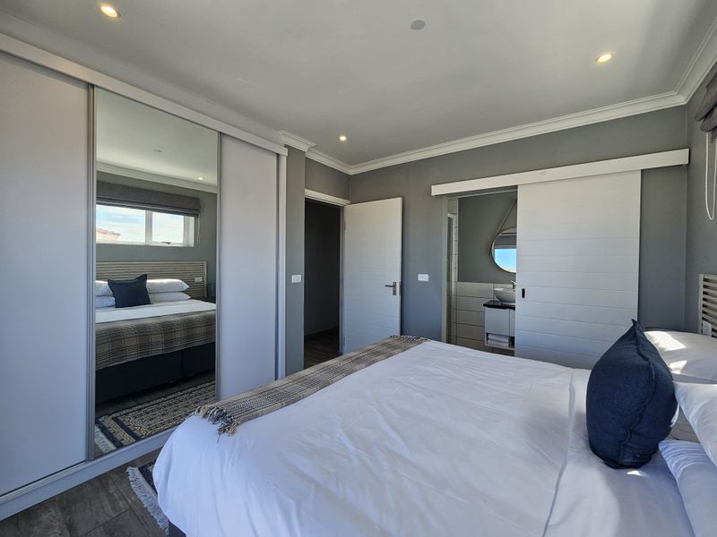 A well-maintained bedroom featuring a large built-in mirrored wardrobe, recessed lighting, and direct access to an en-suite bathroom with modern sliding door.