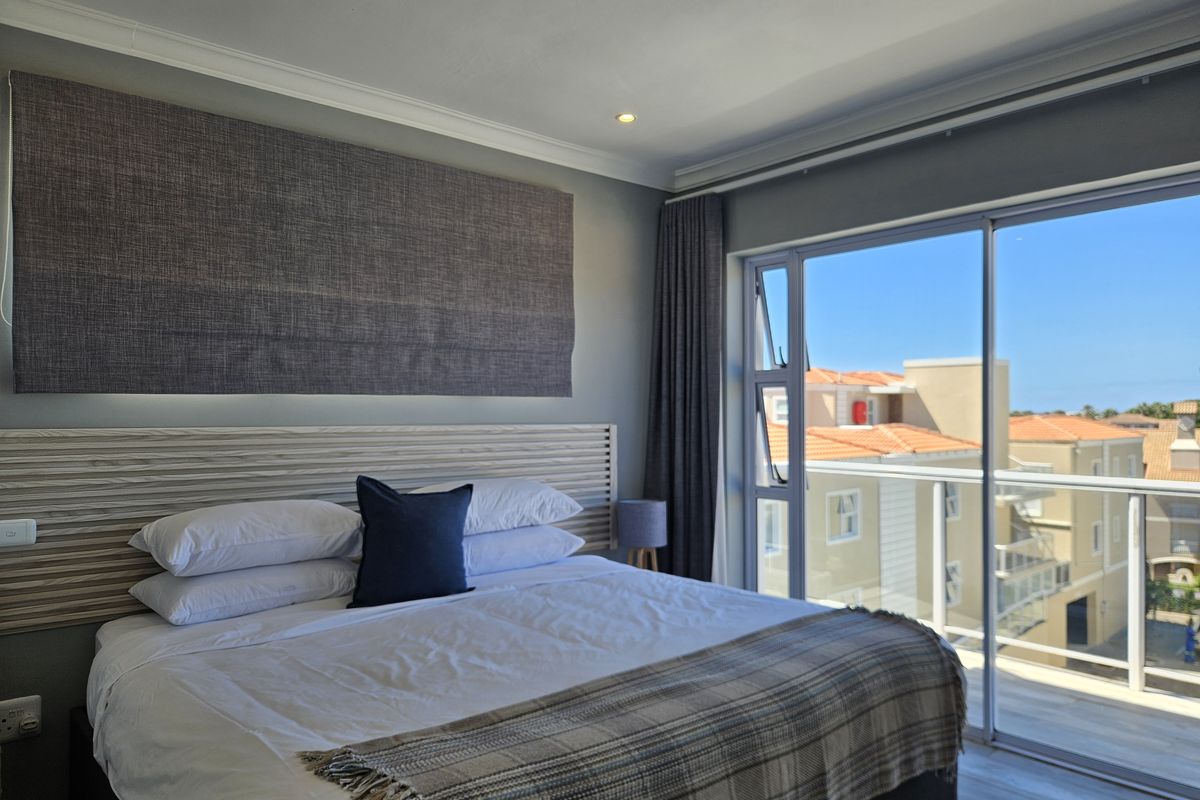 A well-maintained bedroom featuring a built-in headboard, recessed lighting, and large sliding glass doors providing access to a balcony with neighborhood views.