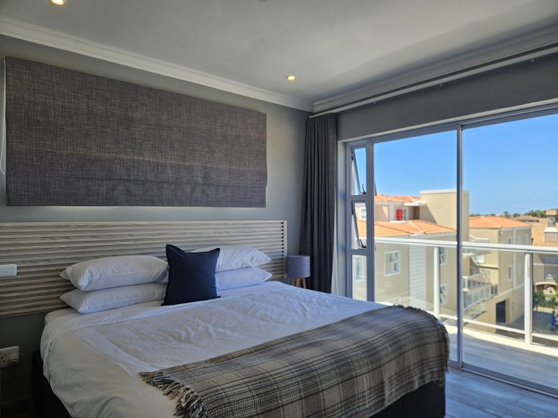 A well-maintained bedroom featuring a built-in headboard, recessed lighting, and large sliding glass doors providing access to a balcony with neighborhood views.