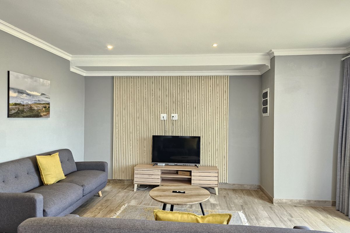 A well-maintained living room featuring a modern timber slat feature wall, recessed downlighting, decorative crown molding, and neutral tiled flooring.