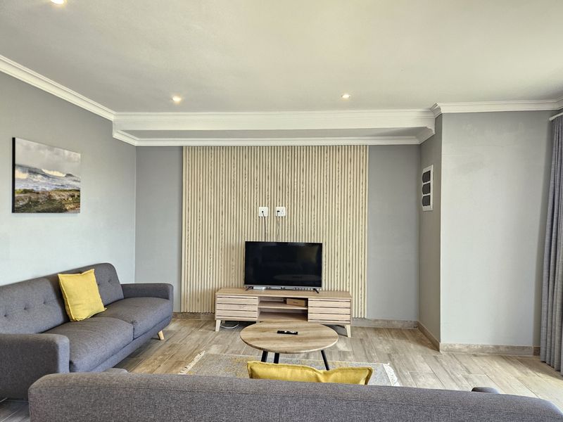 A well-maintained living room featuring a modern timber slat feature wall, recessed downlighting, decorative crown molding, and neutral tiled flooring.