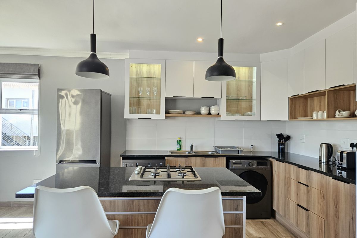 Modern kitchen featuring a central island with a gas hob, sleek wood-tone and white cabinetry, stone countertops, and contemporary pendant lighting.