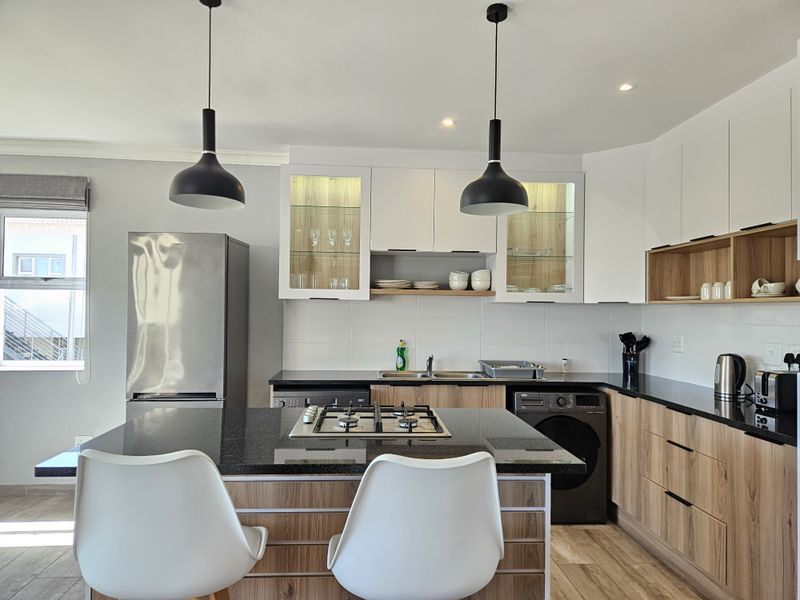 Modern kitchen featuring a central island with a gas hob, sleek wood-tone and white cabinetry, stone countertops, and contemporary pendant lighting.