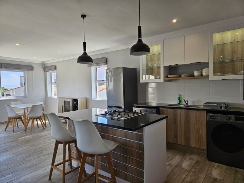 Modern open-plan kitchen and dining area featuring a central island with gas hob, contemporary cabinetry, and wood-look tiled flooring.