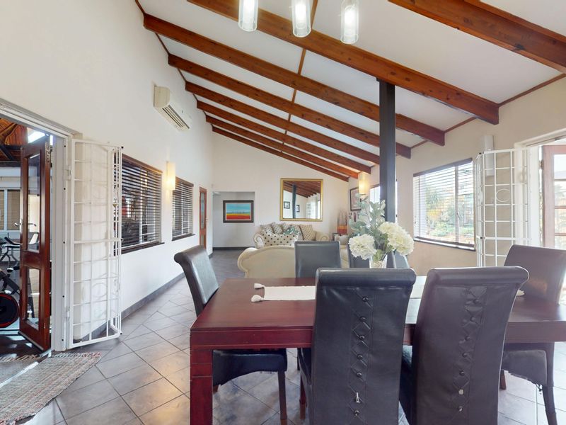 Spacious open-plan living and dining area featuring vaulted ceilings with exposed timber beams, tiled flooring, and direct access to outdoor spaces.