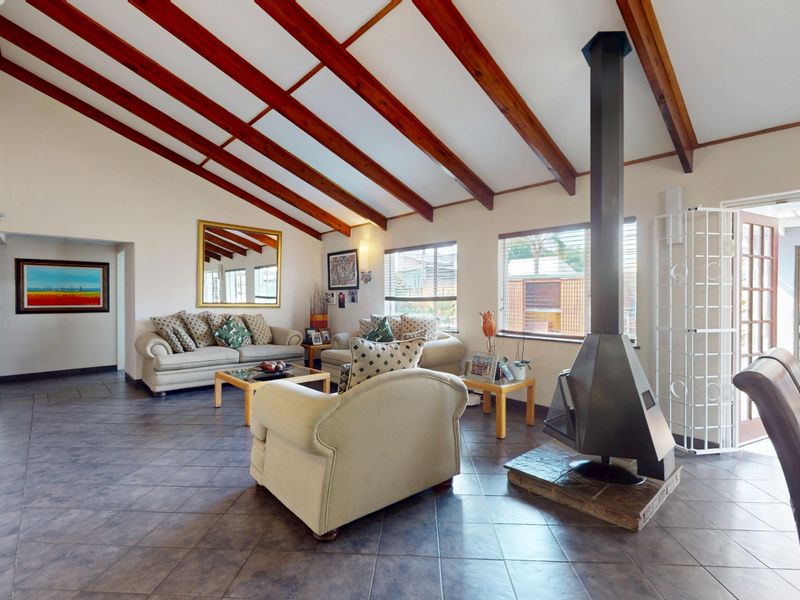 Spacious living room featuring vaulted ceilings with exposed timber beams, tiled flooring, and a prominent freestanding metal fireplace.