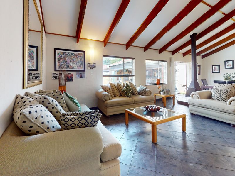 Spacious open-plan living area featuring exposed timber ceiling beams, tiled flooring, and a central freestanding fireplace, creating a warm and inviting atmosphere.