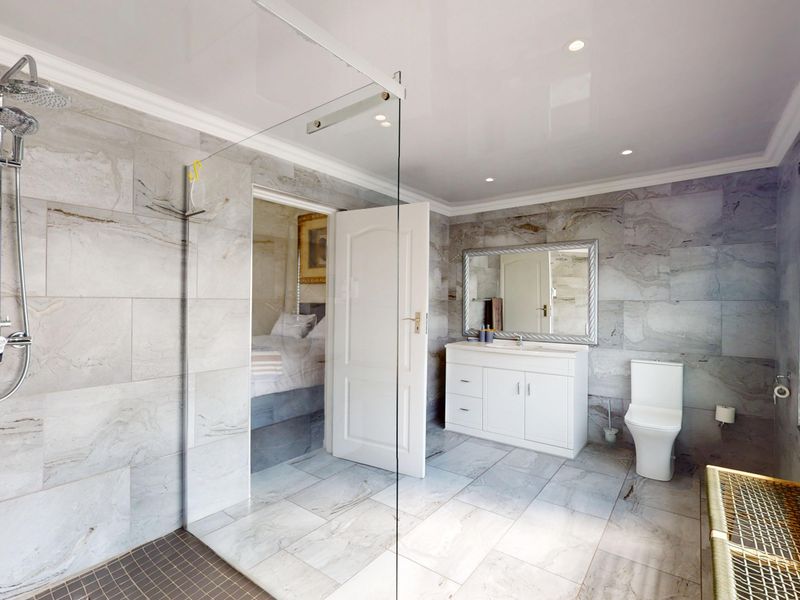 Modern bathroom featuring a spacious walk-in shower with glass screen, vanity unit with basin, and contemporary wall and floor tiling.