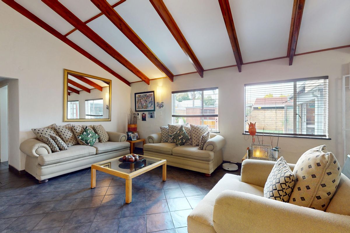 A spacious living room featuring exposed timber ceiling beams, tiled flooring, and large windows that provide ample natural light.