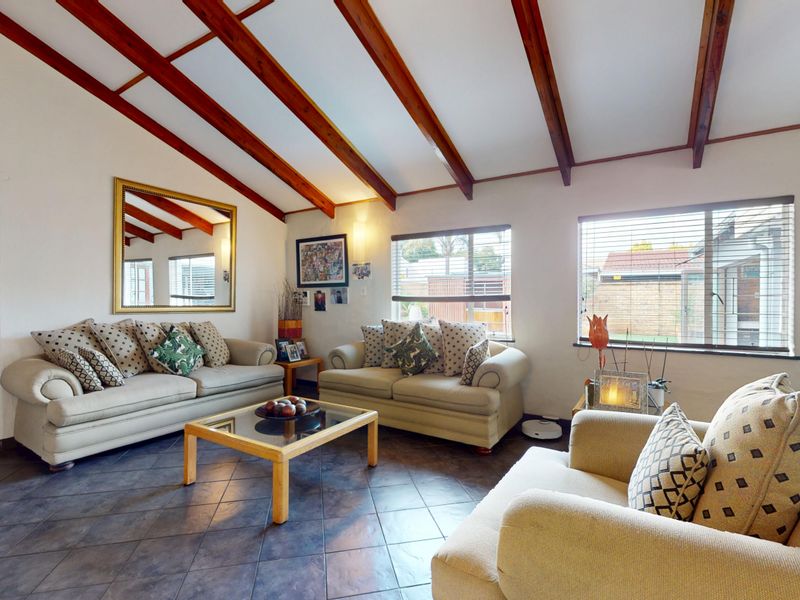 A spacious living room featuring exposed timber ceiling beams, tiled flooring, and large windows that provide ample natural light.