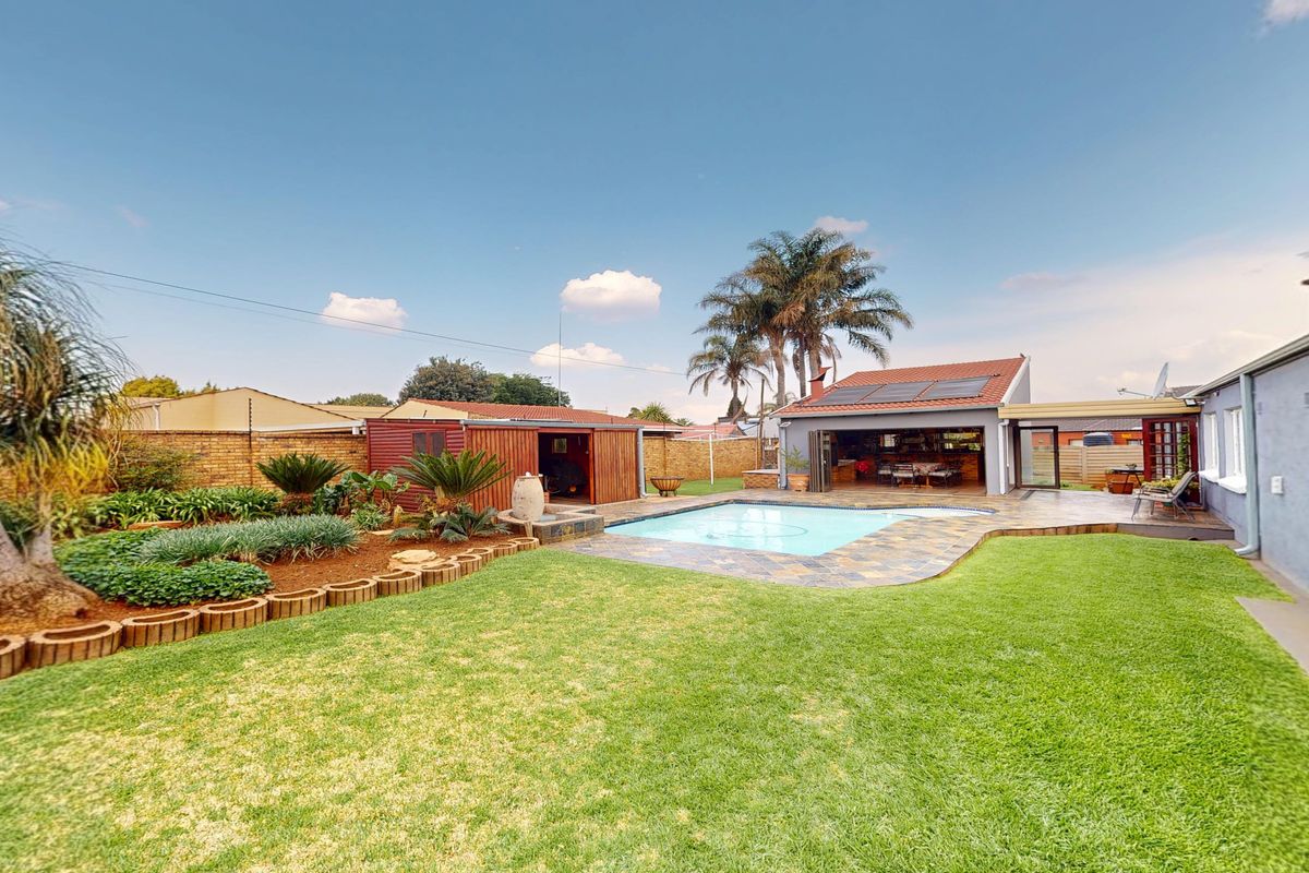 Spacious rear garden featuring a swimming pool, stone paved deck, well-maintained lawn, landscaped garden beds, and a detached storage shed.