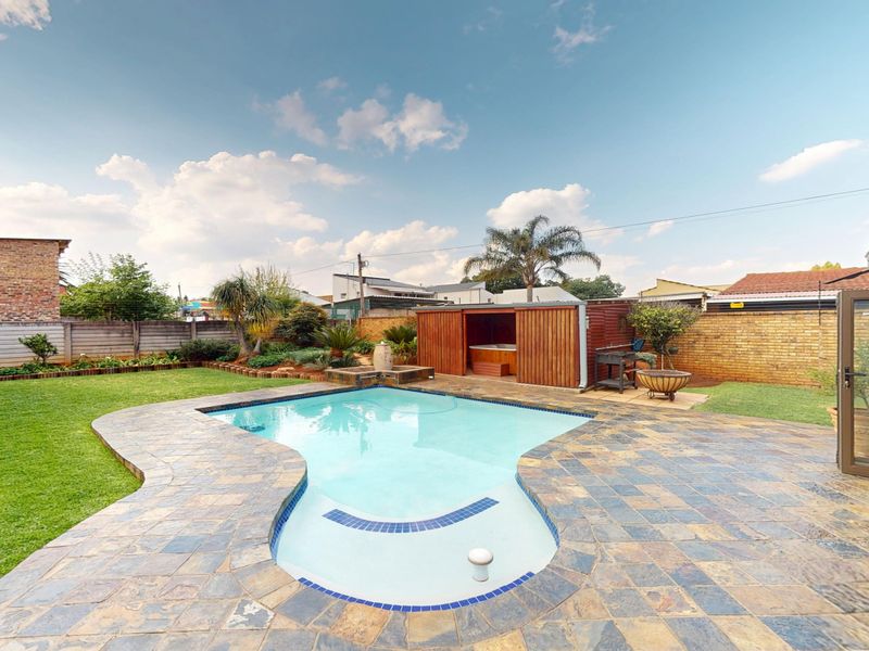 A well-maintained backyard featuring a swimming pool with stone decking, a lawn, and a wooden pool house structure.