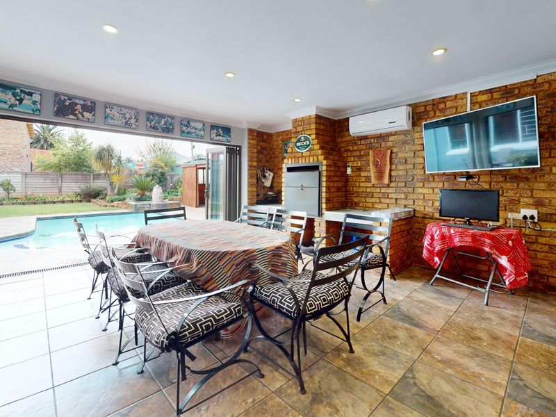 Spacious covered patio featuring a built-in braai, tiled flooring, and large stacking doors that open directly onto the pool area.