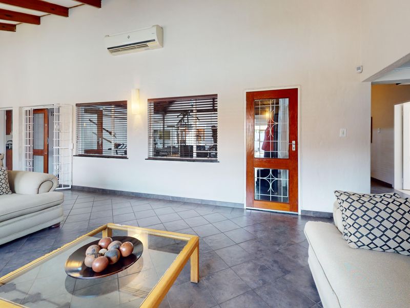 Spacious living room featuring exposed timber ceiling beams, tiled flooring, and a split-system air conditioner, with direct access to adjacent areas.