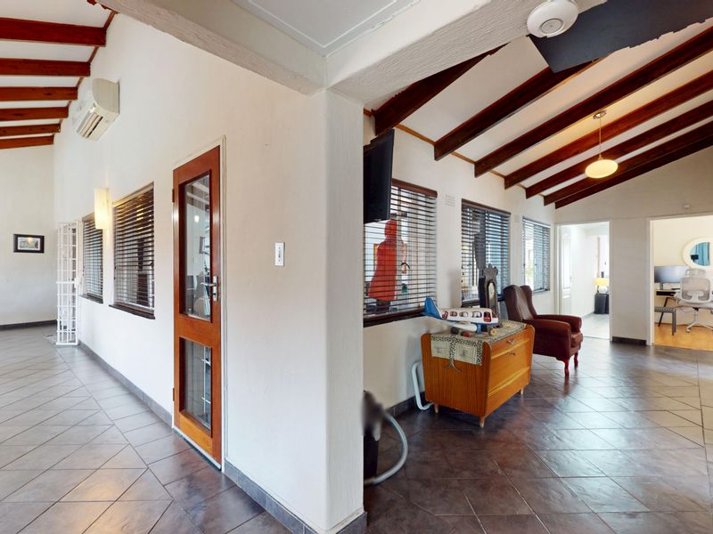 Spacious living area featuring exposed timber ceiling beams, tiled flooring, and large windows with venetian blinds, offering a bright and open layout.
