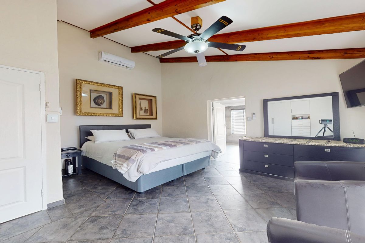 Spacious bedroom featuring exposed timber ceiling beams, tiled flooring, and a split-system air conditioner, offering a comfortable and well-maintained living space.