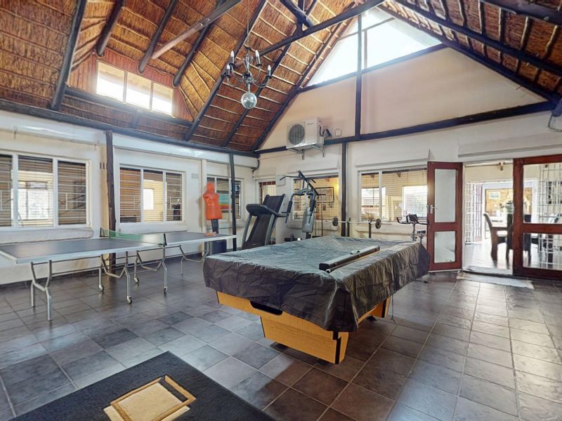 Spacious living area featuring a high vaulted thatched ceiling with exposed timber trusses, tiled flooring, and large windows providing ample natural light.