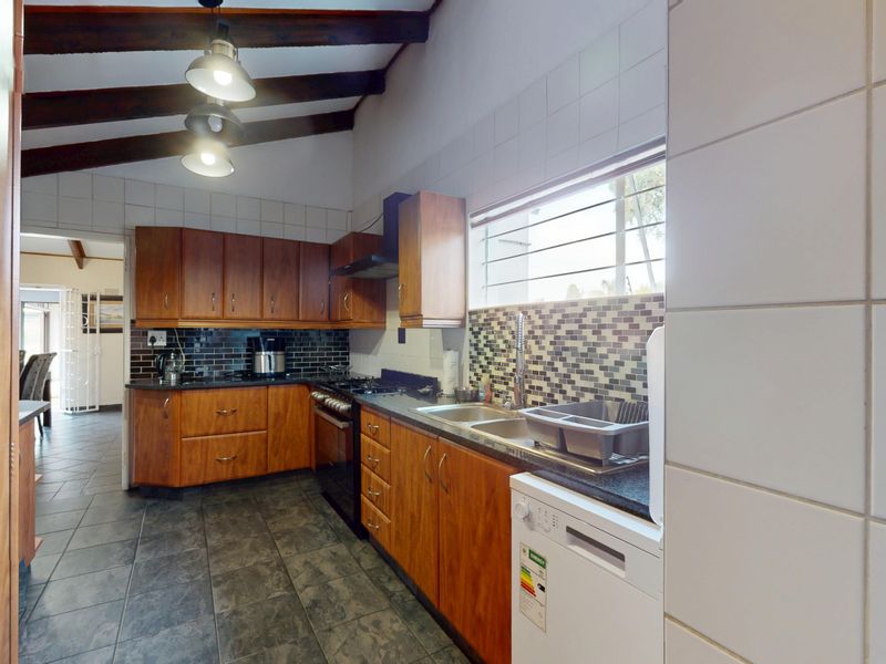 A functional kitchen featuring wooden cabinetry, exposed timber ceiling beams, mosaic tile backsplash, and tiled flooring with integrated cooking appliances.