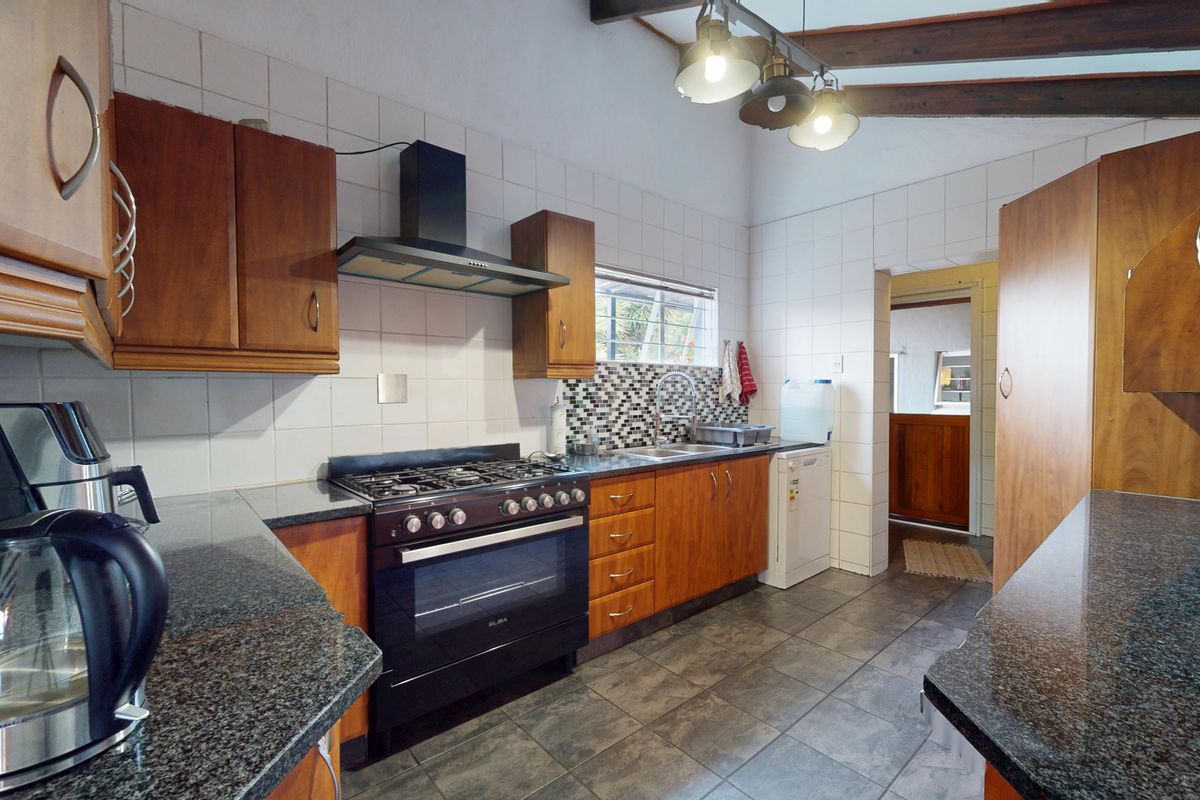 A functional kitchen featuring wooden cabinetry, granite countertops, a gas stove with extractor fan, and tiled finishes with exposed ceiling beams.