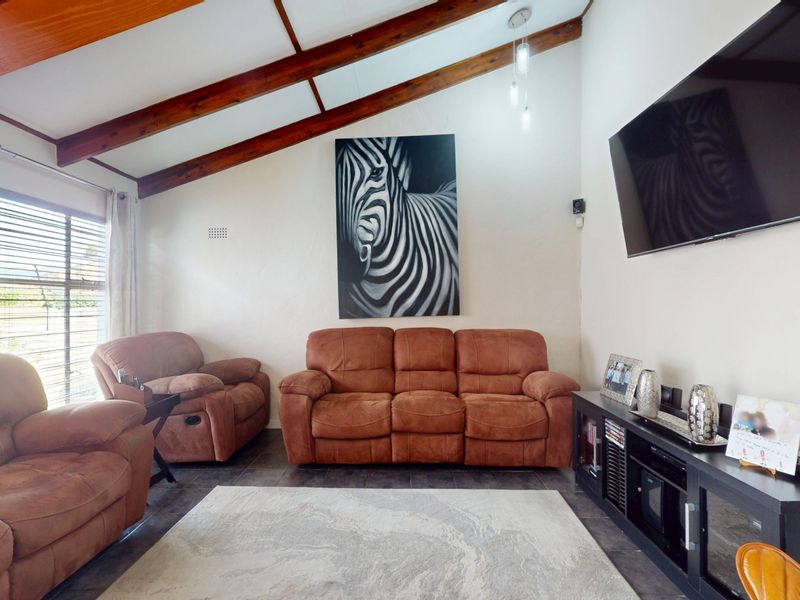 A living room featuring a vaulted ceiling with exposed timber beams and tiled flooring, providing a spacious and character-filled atmosphere.