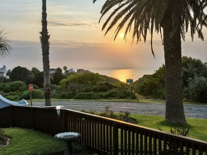 A scenic sunset view overlooking the coastline, featuring a well-maintained garden and timber balustrade in the foreground.