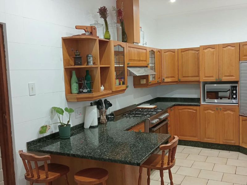 A functional kitchen featuring wooden cabinetry, granite countertops, a gas hob with extractor, and built-in appliances, offering a classic and practical cooking space.