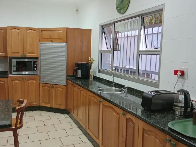 A functional kitchen featuring wooden cabinetry, granite countertops, a stainless steel sink, and tiled flooring, offering a practical workspace with natural light.