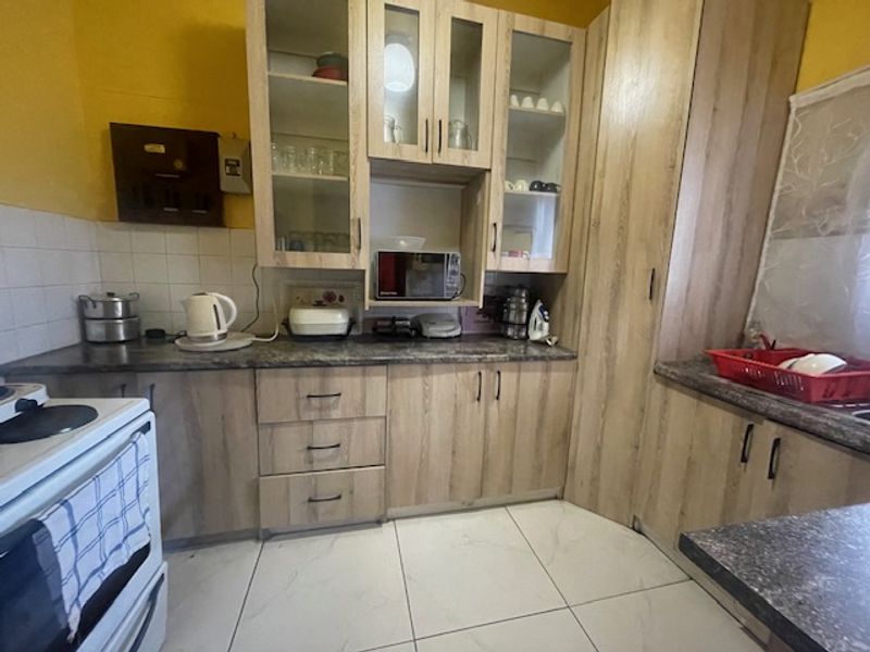 A functional kitchen featuring light wood-finish cabinetry, laminate countertops, tiled backsplash, and tiled flooring, providing ample storage and workspace.