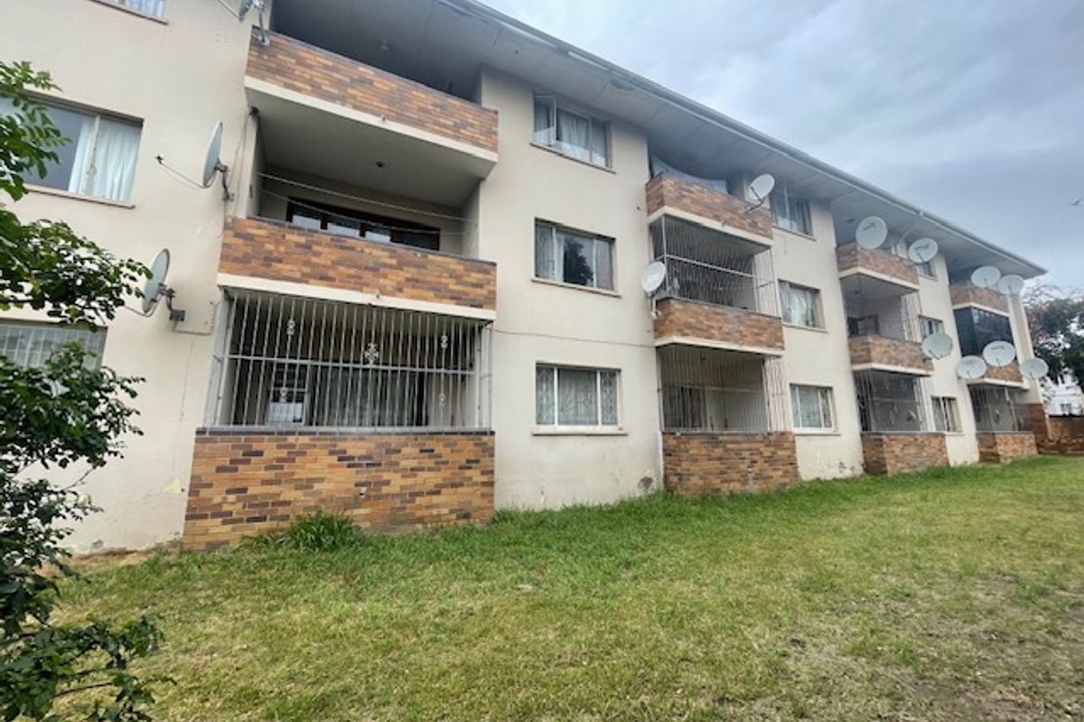 Rear elevation of a multi-story apartment block featuring brick-faced balconies, security bars on lower levels, and multiple satellite dish installations.