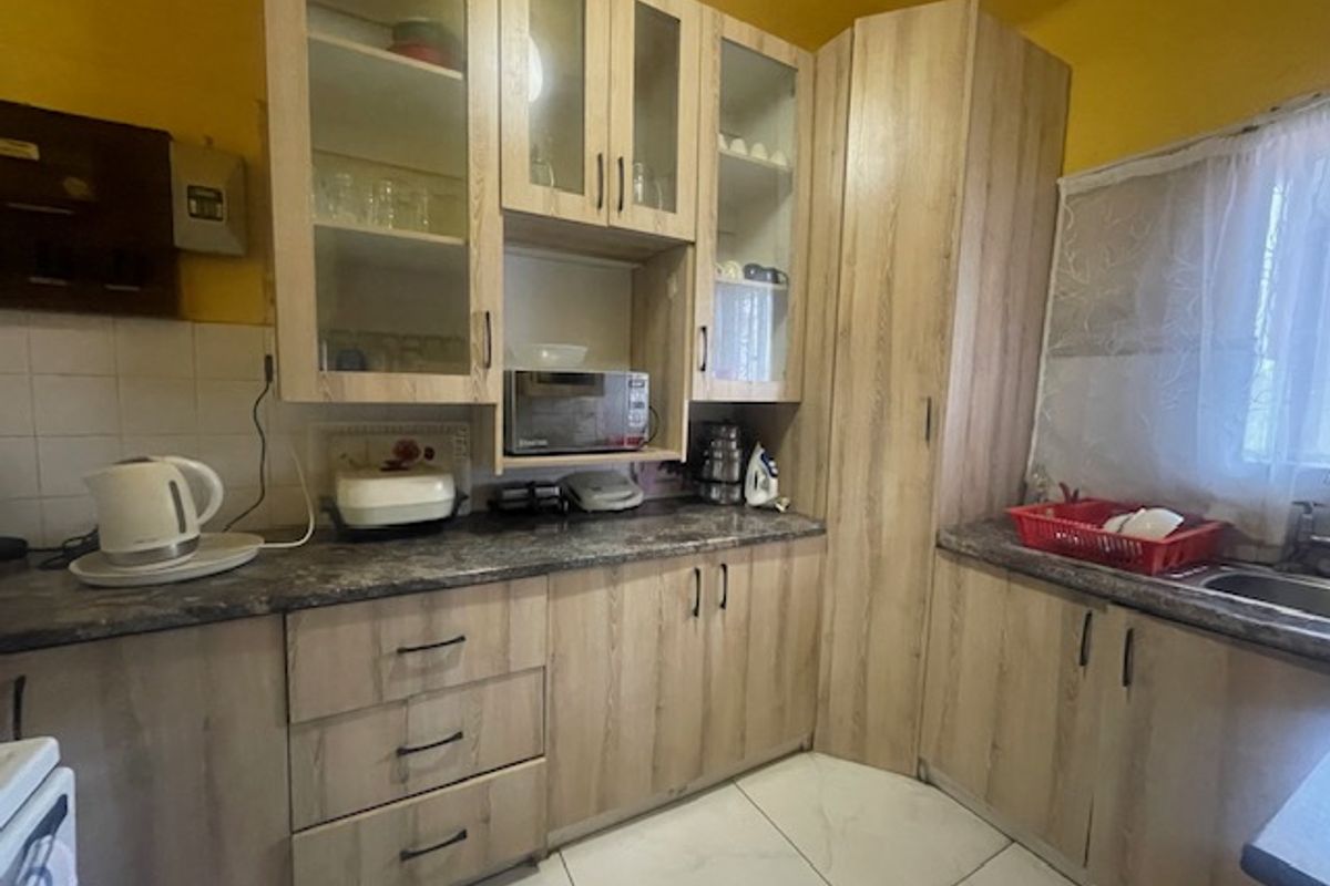 A functional kitchen featuring light wood-look laminate cabinetry, ample storage, tiled backsplash, and tiled flooring, providing a practical workspace for daily meal preparation.