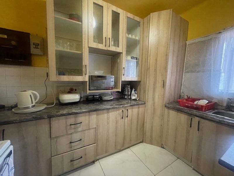 A functional kitchen featuring light wood-look laminate cabinetry, ample storage, tiled backsplash, and tiled flooring, providing a practical workspace for daily meal preparation.