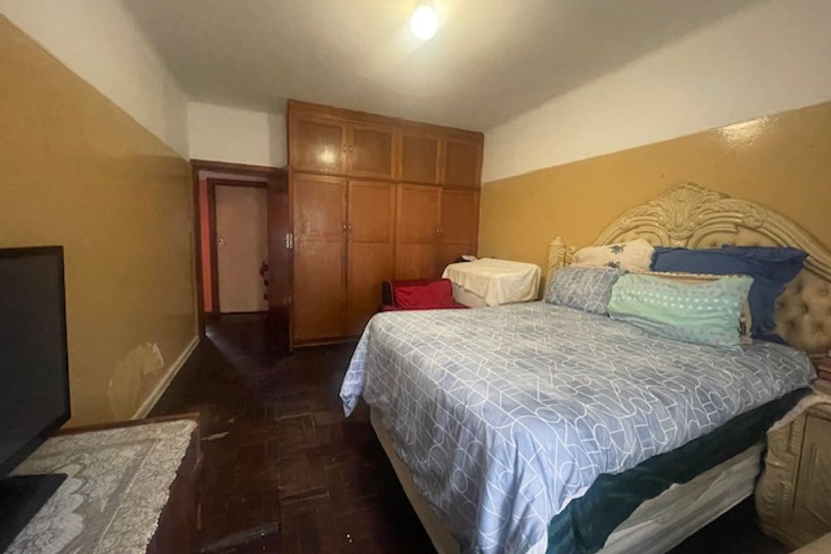 A bedroom featuring built-in wooden cupboards and parquet flooring, requiring cosmetic updates to the wall finishes and general maintenance.
