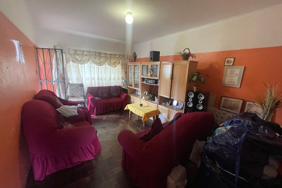 A living room featuring traditional parquet flooring and a security gate, currently requiring cosmetic updates to the wall finishes.