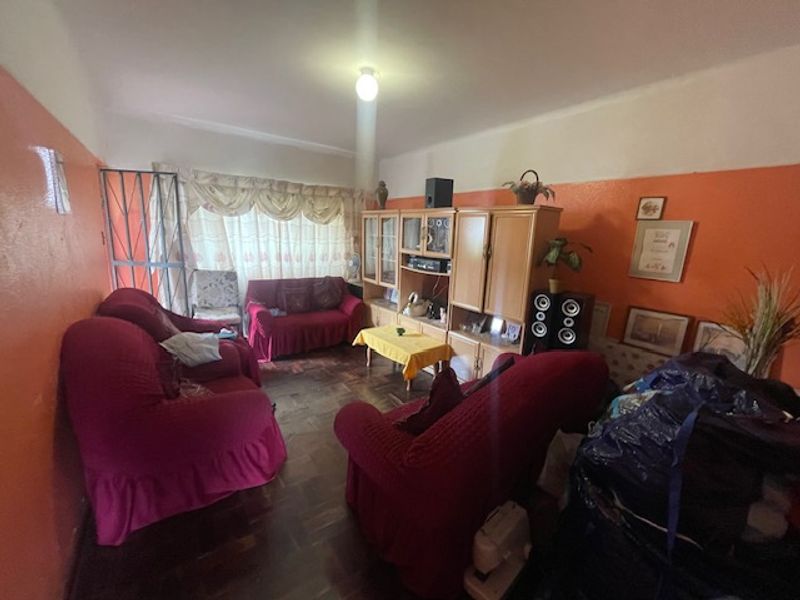 A living room featuring traditional parquet flooring and a security gate, currently requiring cosmetic updates to the wall finishes.